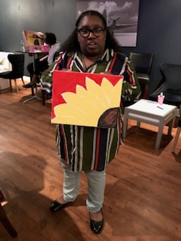 A guest holding a sunflower painting at a STAMP Love paint night